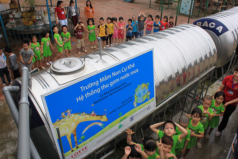 children gathered around large metal water tanks