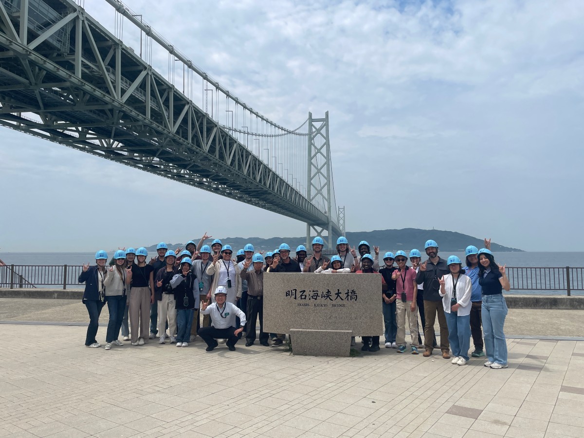 A cohort of UT students and Professor of Practice Gregory Brooks standing under Akashi Kaikyo bridge in Japan with Satoshi Kashima