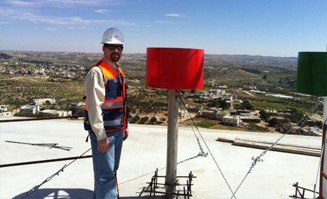 Greg Kolenovsky in construction hard hat and sunglasses on roof of building overlooking coutryside