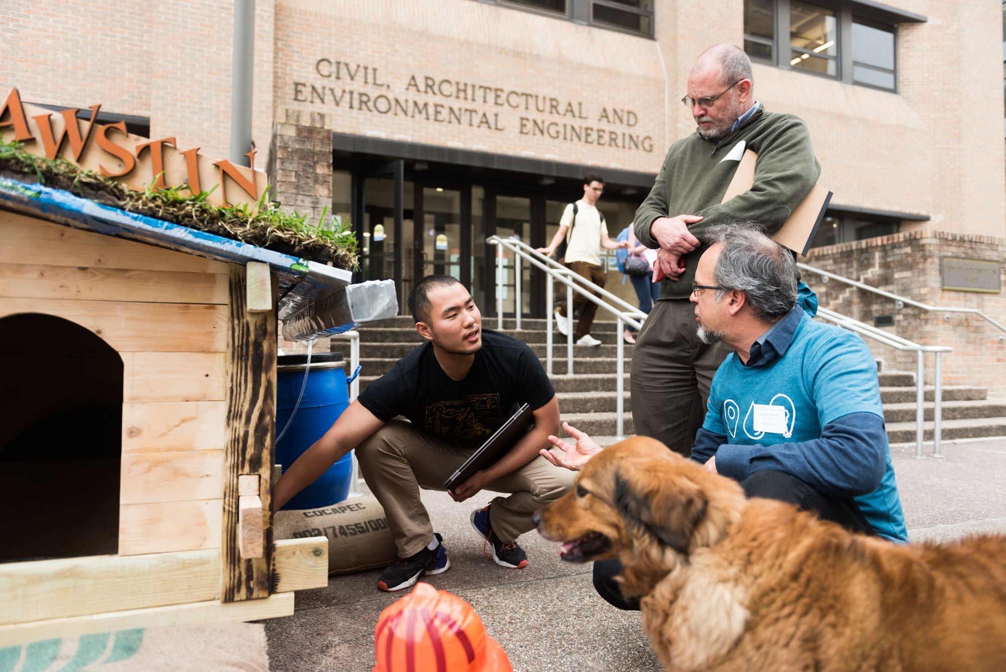Student showing his sustainable doghouse design to judges and a dog