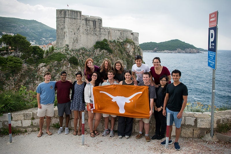 Texas Engineering students smiling on a bridge while holding a UT Austin flag
