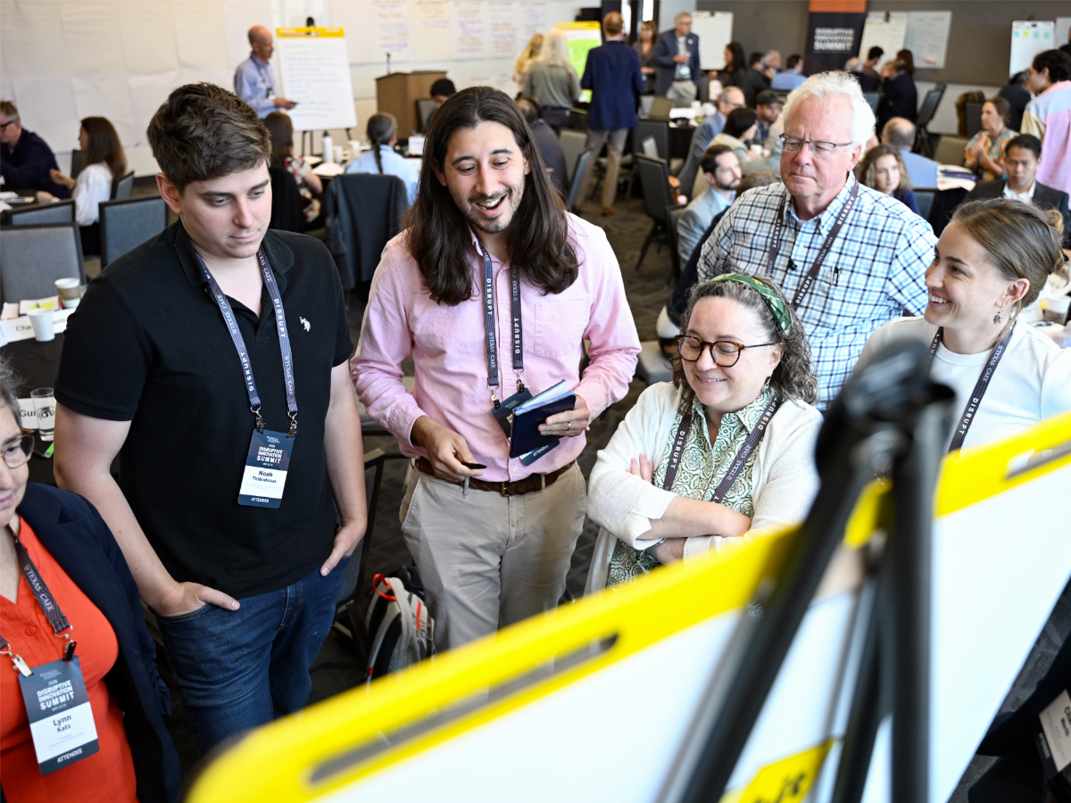 Group of people looking at research poster and talking at 2026 CAEE Disruptive Innovation Summit event.
